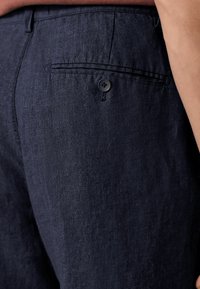 Pantalons en lin bleu marine avec une poche arrière dotée d'un bouton noir et d'une texture subtile, au design ajusté et aux lignes épurées.