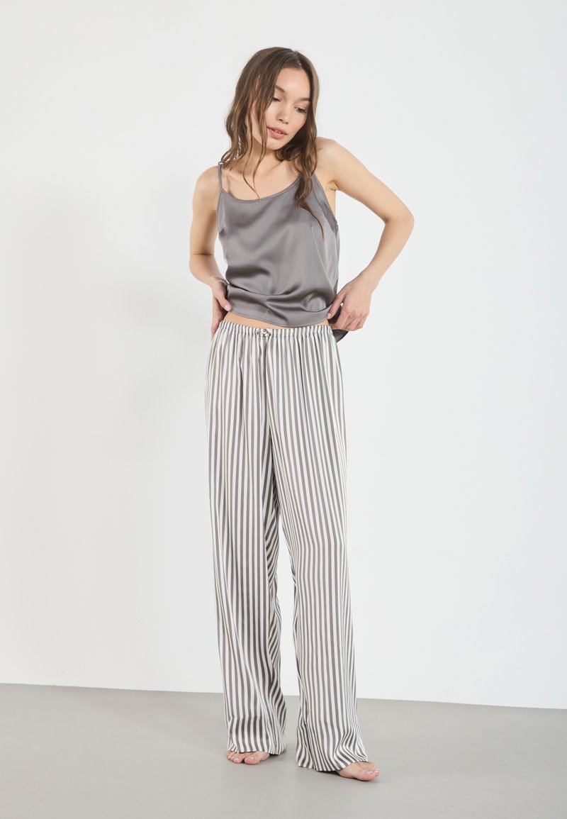 Haut camisole en satin gris associé à un pantalon ample à rayures verticales blanches et grises. Le tissu semble lisse avec une texture douce.