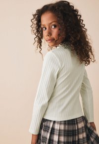 Top de manga larga verde claro acanalado con diseño ajustado, combinado con una falda a cuadros en blanco y negro. Tejido con textura, escote estándar.