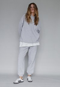 Szara bluza z kapturem i pasujące spodnie dresowe z elastycznymi mankietami; nałożone na biały top. Czarno-białe sneakersy dopełniają casualowy wygląd.