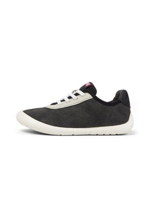 Zapatilla deportiva de ante negro con suela y cordones blancos, ribete gris claro y etiqueta roja en la lengüeta negra, mostrada de lado sobre fondo blanco.