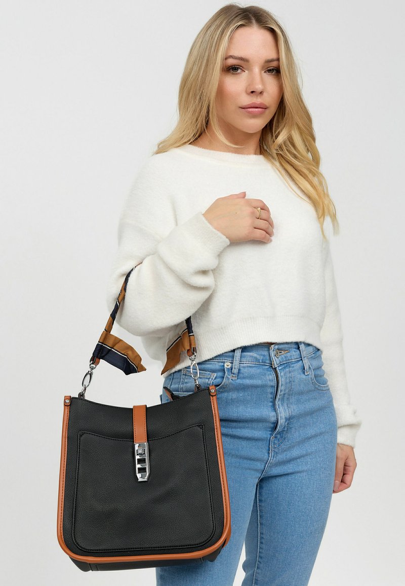 Zwarte leren handtas met een bruin accent en een verstelbare schouderband, voorzien van een voorzak en metallic sluitingdetail.