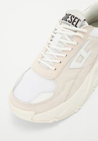 Valge ja hele roosa sneaker, millel on võrkkangas ja nahkpea, ümmargused paelad, paks tall ja logo keelel. Rõhutatud tikanditega detailidega.