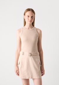 Débardeur beige côtelé associé à une jupe short taille haute, avec poches et une ceinture à boucle ronde. Texture lisse.