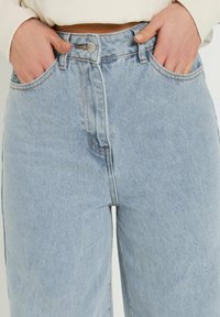 Jeans in denim azzurro chiaro a vita alta con chiusura a bottoni e zip, tasche laterali e dettagli di cucitura a contrasto. Fit a gamba larga.