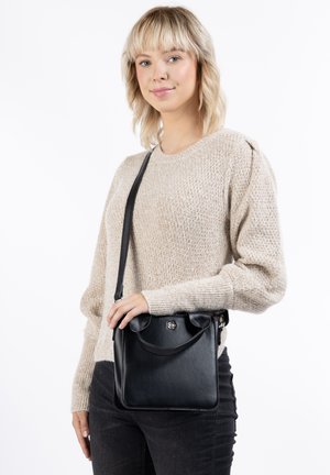 Borsa nera in pelle con una texture liscia, forma sagomata e una piccola maniglia. Presenta una patta frontale con una chiusura metallica.