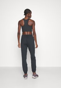Černý sportovní crop top s proužky a odpovídající černé jogger kalhoty, s elastickým pasem, zúženými manžetami a hladkým textilním povrchem.