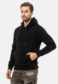Schwarzer Kapuzenpullover aus Baumwollmischung, mit einer vorderen Kängurutasche, Kordelzügen, gerippten Bündchen und lockerer Passform.