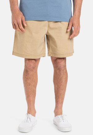 Shorts kaki à coupe droite, fabriqués en mélange de coton lisse, avec un devant plat et des détails de couture discrets. Associés à des baskets blanches.