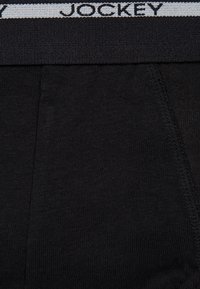 Schwarze Baumwollslips mit breitem Bund, der das graue "JOCKEY"-Logo zeigt, glatte Textur und minimalistisches Design.