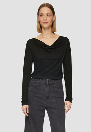 Czarny longsleeve z dekoltem w serek, zestawiony z ciemnoszarymi dżinsami z subtelnymi ćwiekami. Gładki, elastyczny materiał.