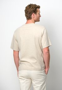 Beige t-shirt med kort ärm, avslappnad passform, rund halsringning och mjuk textur. Bärs med ljusa bomullbyxor.