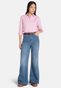 Ljusrosa långärmad skjorta med knappar, i kombination med högmidjade, vida blå denimjeans. Brunt läderbälte och bruna platåskor.