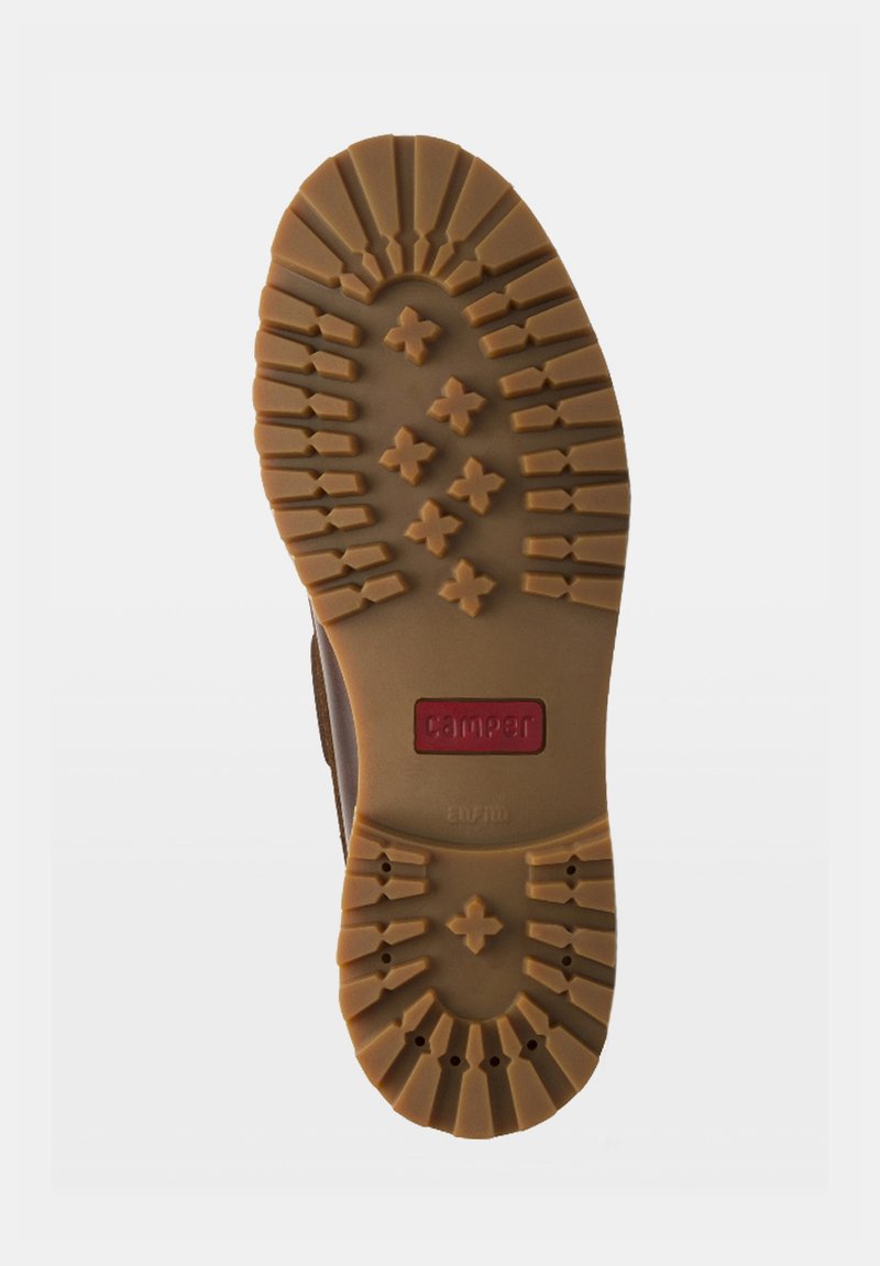 Semelle d'une chaussure marron avec des rainures profondes, des motifs en forme de croix, et un logo rectangulaire rouge portant l'inscription "camper" au centre.