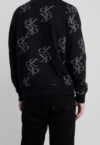 Felpa nera con motivo all-over del logo CK in grigio. Presenta polsini e orlo a coste, texture morbida e vestibilità rilassata.