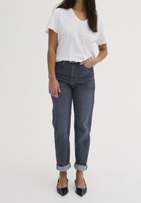 T-shirt bianco a scollo a V abbinato a jeans blu scuro con risvolti e tacchi a punta neri, con una vestibilità aderente e texture in denim.