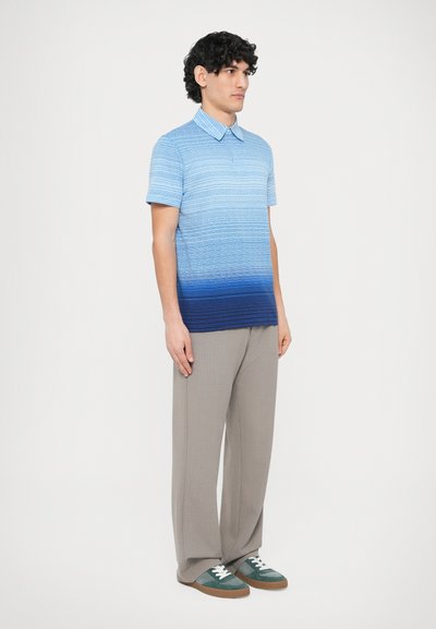 Modré polokošeľa s prechodom farby a horizontálnymi pruhmi, krátkymi rukávmi a golierom; v kombinácii s svetlosivými nohavicami a teniskami so zelenými detailmi.