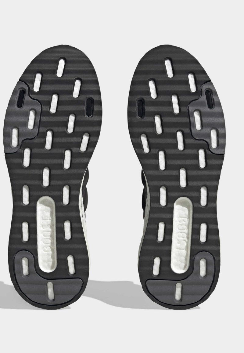 Schwarze und weiße Sneakersohle aus strukturiertem Gummi, mit kreisförmigen und ovalen Ausschnitten sowie einer dicken, gepolsterten Sohle.