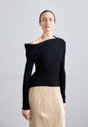 Black ribbed off-shoulder top with long sleeves, paired with a pleated beige skirt. The top features a draped design for added texture.