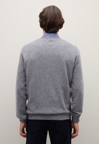 Maglione grigio a maglia con collo rotondo e polsini a costine, caratterizzato da una consistenza morbida e una vestibilità comoda, indossato sopra una camicia a righe blu.