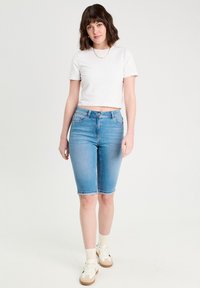 Shorts en denim bleu clair, de coupe bermuda mi-haute, dotés de cinq poches et d'ourlets retroussés, associés à un t-shirt blanc uni cropped.