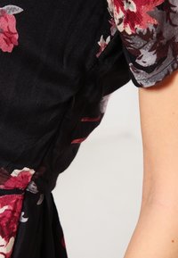 Robe noire à motifs floraux, avec une texture douce, des manches courtes et de vives fleurs rouges et blanches, dotée d'une taille cintrée.