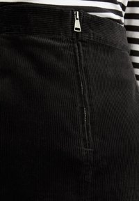 Gonna di velluto a coste nera con texture a coste verticali, dotata di una zip metallizzata sul davanti. Abbinata a una maglia a righe bianco e nera.