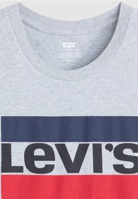 T-shirt en coton gris avec un large design horizontal comportant des rayures bleu marine et rouges, affichant en évidence le logo "Levi's" en lettres noires en gras.
