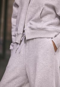 Felpa con cappuccio grigia chiara e pantaloni della tuta realizzati in un morbido tessuto texturizzato. Presenta tasche laterali, chiusura con zip e un discreto dettaglio ricamato del marchio.