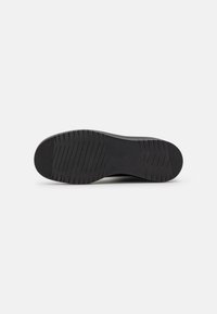 Semelle de chaussure en caoutchouc noir avec des rainures texturées pour l'adhérence, des bords lisses et une légère courbe au niveau du talon pour la stabilité.