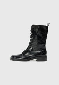 Bottes noires en cuir à cheville avec une finition brillante, dotées d'un laçage à l'avant, d'un bout arrondi et d'un petit talon bloc. Détails de couture visibles.