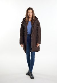 Brown insulated parka with a hood, featuring zippered pockets, paired with a light blue top, blue jeans, and black ankle boots.