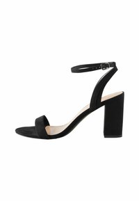 Sandale à talons hauts en daim noir avec une large lanière sur les orteils, une lanière réglable autour de la cheville et un talon bloc. Texture lisse.