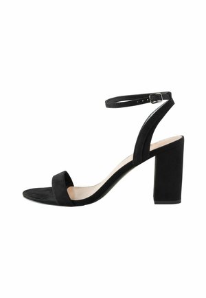 Sandale à talons hauts en daim noir avec une large lanière sur les orteils, une lanière réglable autour de la cheville et un talon bloc. Texture lisse.