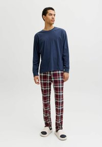 Chemise manches longues bleu marine associée à un pantalon de pyjama à carreaux rouges et à des chaussures beige à enfiler. Les pantalons présentent des accents blancs et bleus dans le motif.