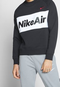 Nike Air sweatshirt i svart med en vit central panel som har fet svart text. Designen inkluderar en liten röd logotyp på axeln.
