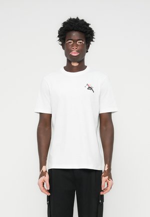 Weißes Baumwoll-T-Shirt mit kurzen Ärmeln, Rundhalsausschnitt, mit einem kleinen grafischen Motiv einer springenden Figur in Rot und Schwarz auf der Brust.