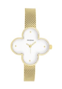 Montre-bracelet en maille dorée avec un cadran blanc en forme de trèfle, comportant des index et aiguilles dorés, ainsi qu'une petite couronne sur le côté.