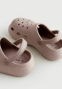 Ljusrosa gummiträskor med ventilationshål, justerbar bakkappa och strukturerade sulor, med en rundad form och slät yta.