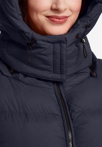 Navyblauwe pufferjack met een hoge kraag, verstelbare toggles, staande rits en een gequiltde textuur.