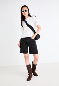 White short-sleeve t-shirt, black denim shorts, and brown leather knee-high boots. Accessories include a black crossbody bag and sunglasses.