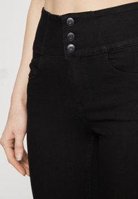 Černé jeansy s vysokým pasem, které mají tři knoflíkové zapínání, klasický design se pěti kapsami a hladký, elastický materiál.