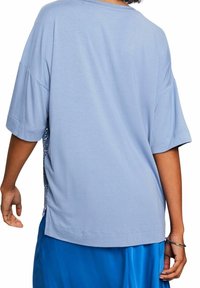 Persona vestida con una camiseta holgada de manga corta azul claro con lentejuelas en los laterales y una falda azul brillante, vista desde la espalda.