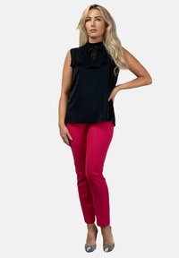 Czarny bezrękawnik z falbaniastym kołnierzem i dekoracyjnymi zdobieniami, w połączeniu z jaskraworóżowymi dopasowanymi spodniami i wzorzystymi szpilkami.