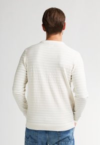 Licht crèmekleurige trui met verticale ribbelstructuur, ronde halslijn en lange mouwen. Katoenmixstof zorgt voor een zachte, gladde feel.