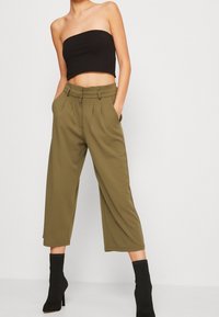 Skrócony czarny top bez ramiączek w połączeniu z oliwkowymi spodniami typu wide-leg z plisami i paskiem w talii. Czarna, teksturowana botki do kostek.