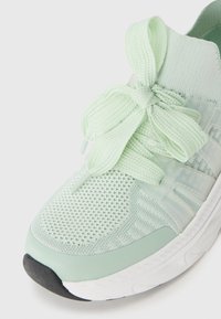 Light mint-green sneaker featuring a textured mesh upper, flat laces, padded collar, and a white rubber sole with a black accent.