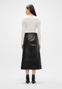 Μαύρη δερμάτινη μίντι φούστα με στενή μέση, που διαθέτει έντονα ραφά και πορτοκαλί ραφή, συνδυασμένη με εφαρμοστό λευκό μπλουζάκι με μακρύ μανίκι και μποτάκια μέχρι τον αστράγαλο.