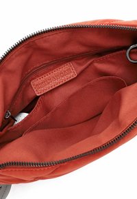 Interior de una bolsa de tela roja con una textura suave. Presenta una etiqueta de cuero "EMILY & NOAH" y un bolsillo con cremallera en el costado.
