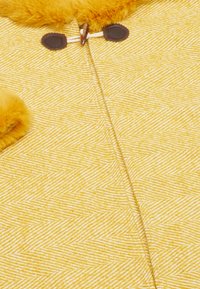 Sárga, textúrált anyag, halszálka mintával, puha szőrmés díszítéssel és sötét gombokkal. A termék melegnek és kényelmesnek tűnik.